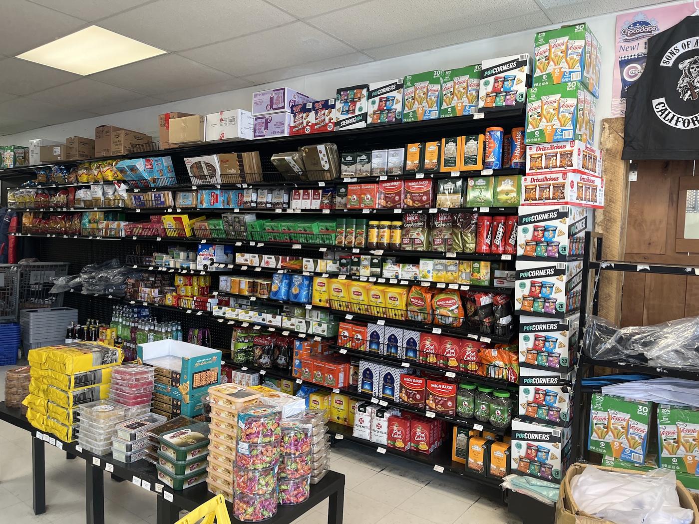 A grocery aisle from floor to ceiling: bays of boxed tea, jars, biscuits and imported snacks, with tubs of wrapped sweets and boxed baklava on the table in front.