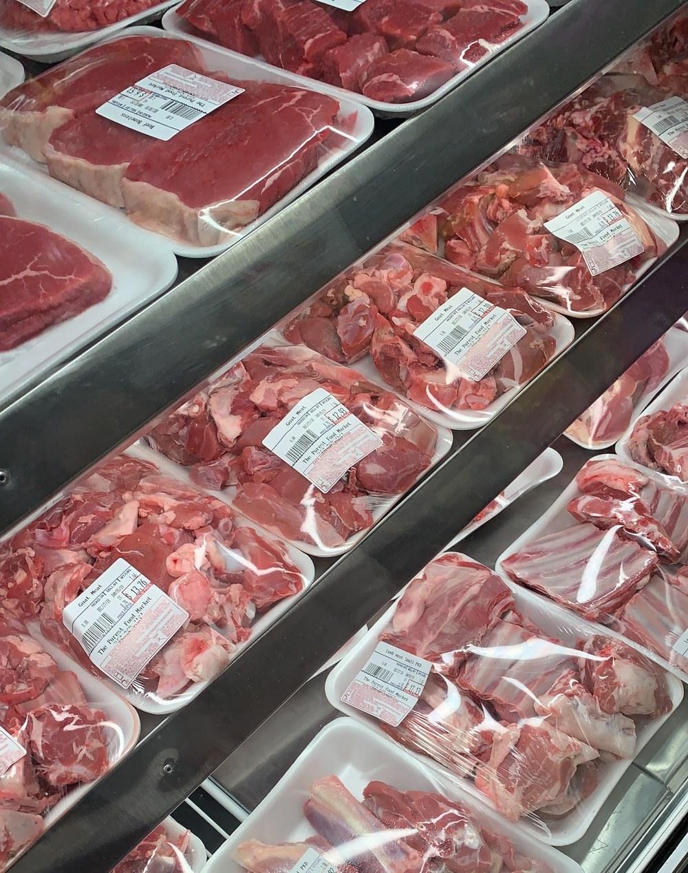 The fresh meat case: trays of goat, lamb and boneless beef wrapped under film, each carrying a scale label printed with the shop's own name.